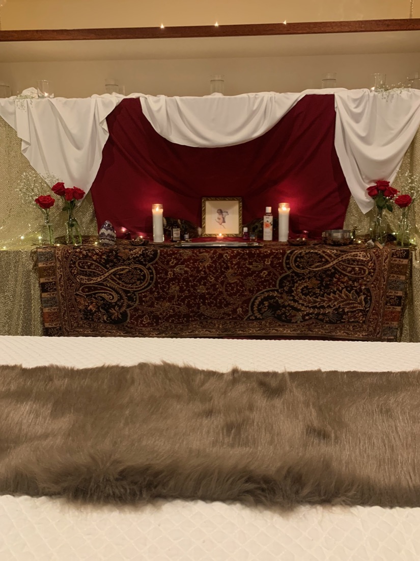A candlelit altar at the foot of a bed
