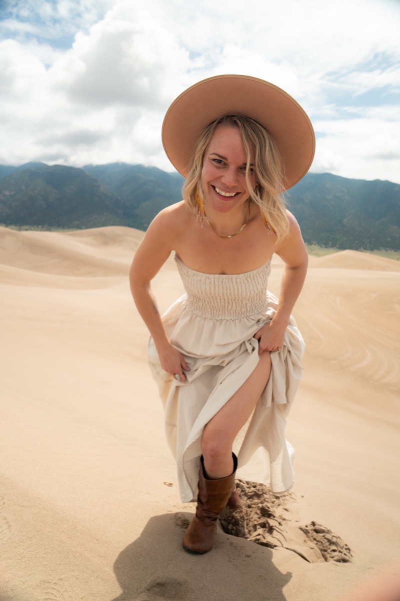 Nicole Marie Rose laughing on the sand dunes in a sun hat